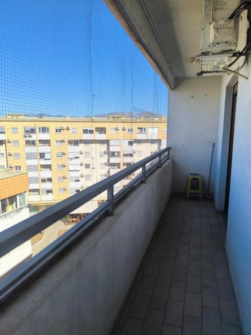Dugačka natkrivena terasa sa zaštitnom mrežom i pogledom na zgradu.