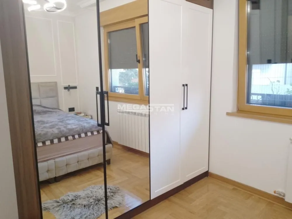 Spavaća soba sa velikim garderoberom sa ogledalom i bračnim krevetom.