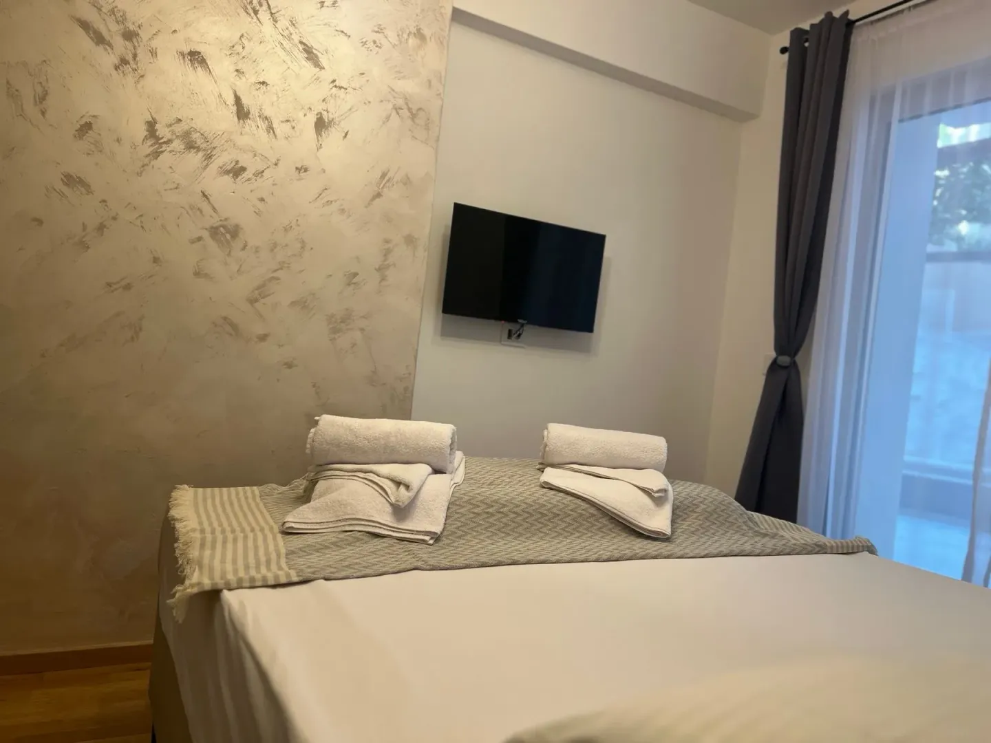 Uređena spavaća soba sa bračnim krevetom, složenim peškirima i televizorom na zidu.