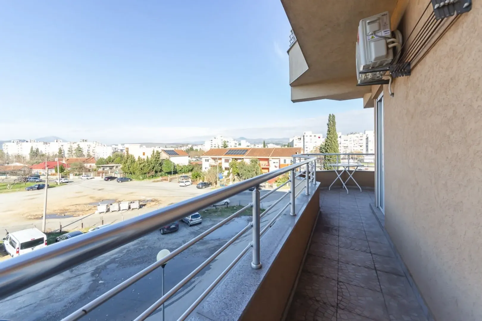 Dugačak balkon sa metalnom ogradom i pogledom na naselje.