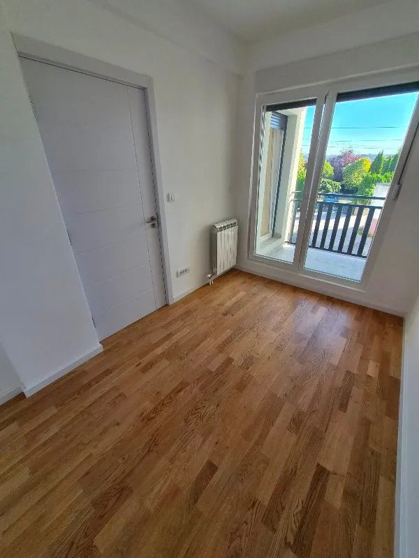Prazna svetla soba sa drvenim podom i izlazom na balkon.