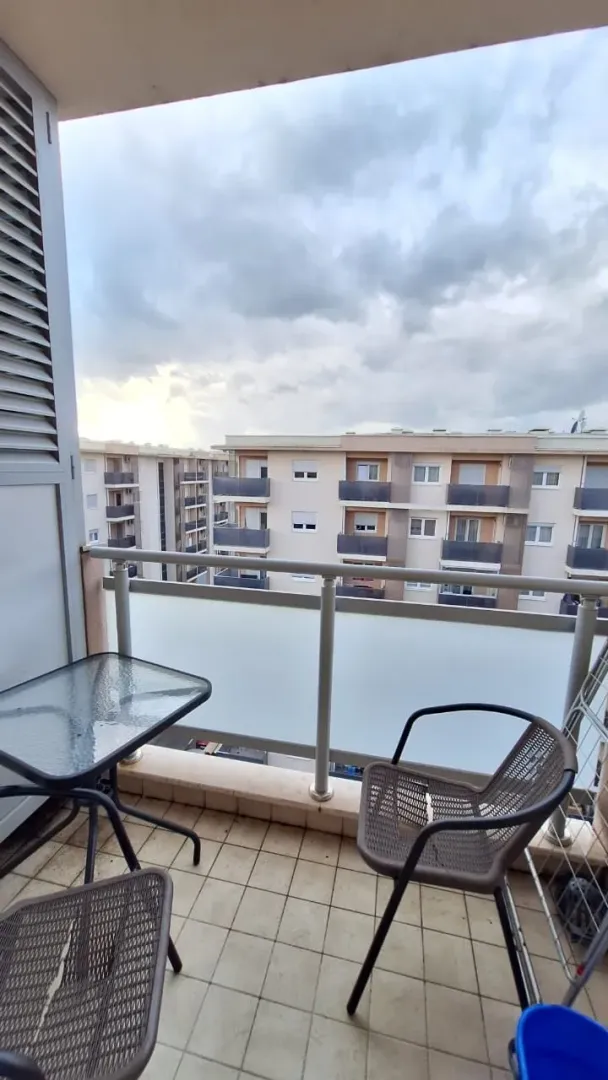 A small furnished balcony with a table, chairs, and a view of surrounding buildings.