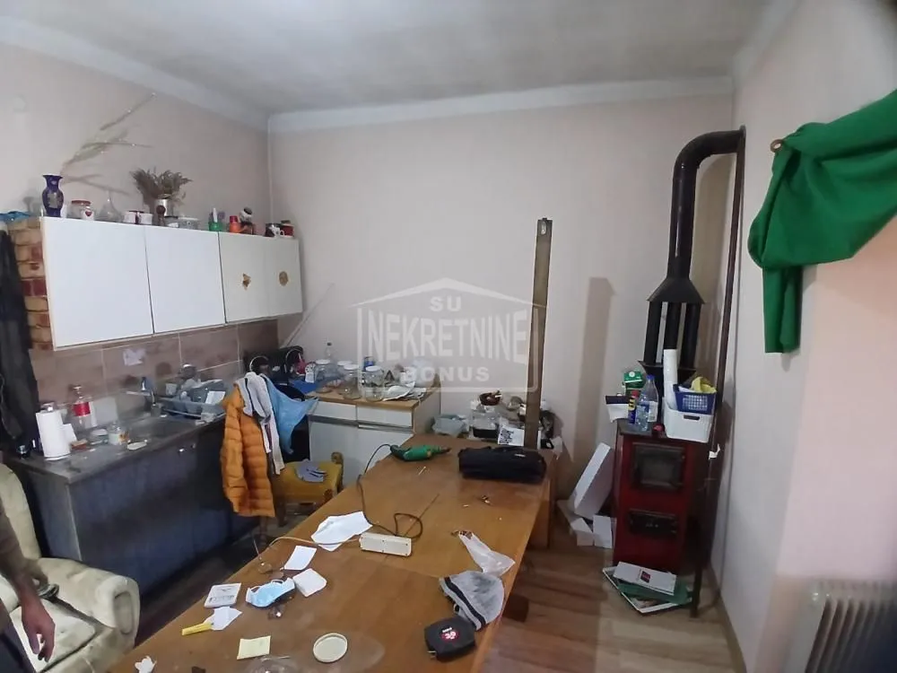 Manja kuhinja sa sudoperom, elementima i pećicom na drva u uglu prostorije.