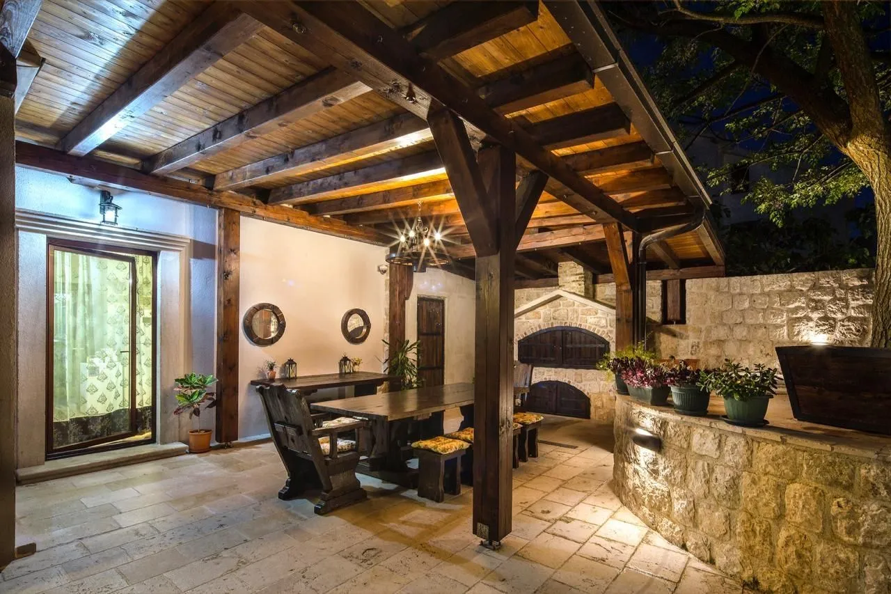 Covered stone terrace with wooden tables and an outdoor fireplace.