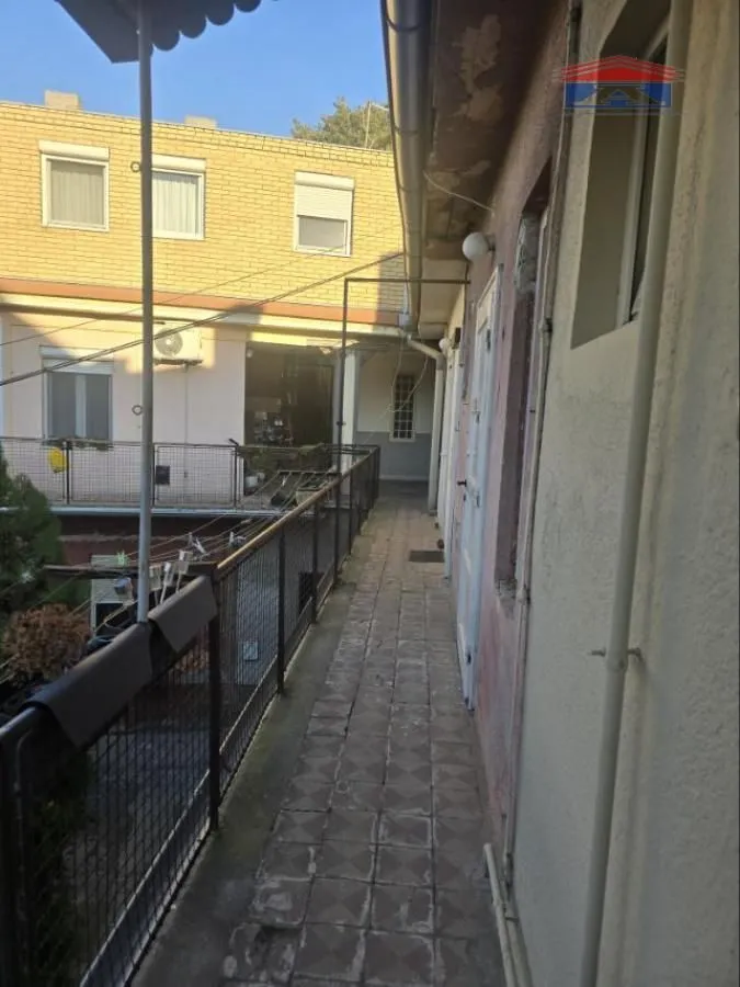 Dugački spoljni hodnik sa popločanim podom i ogradom duž zgrade.