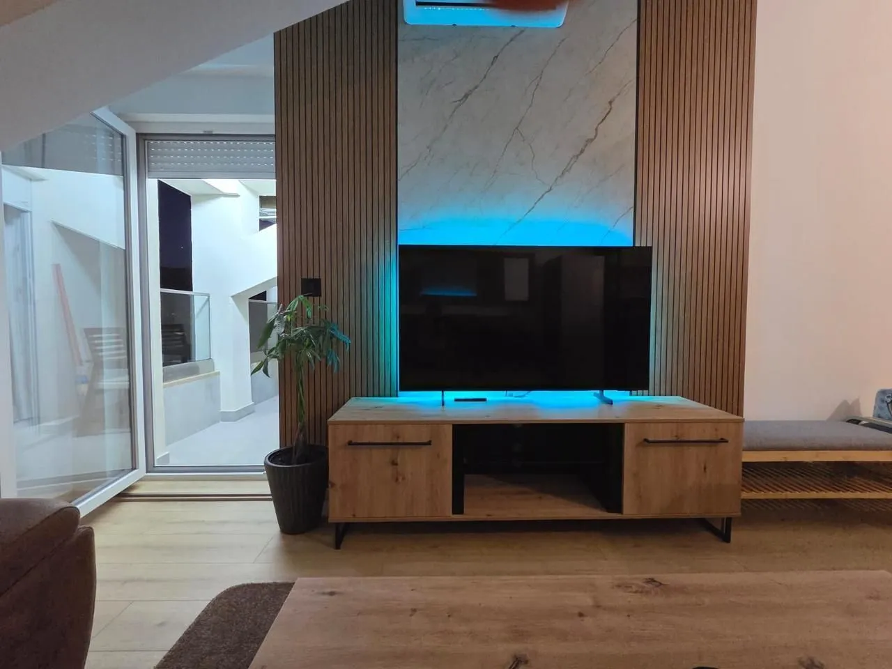 Living room with a television, wooden wall panels, and blue backlighting.