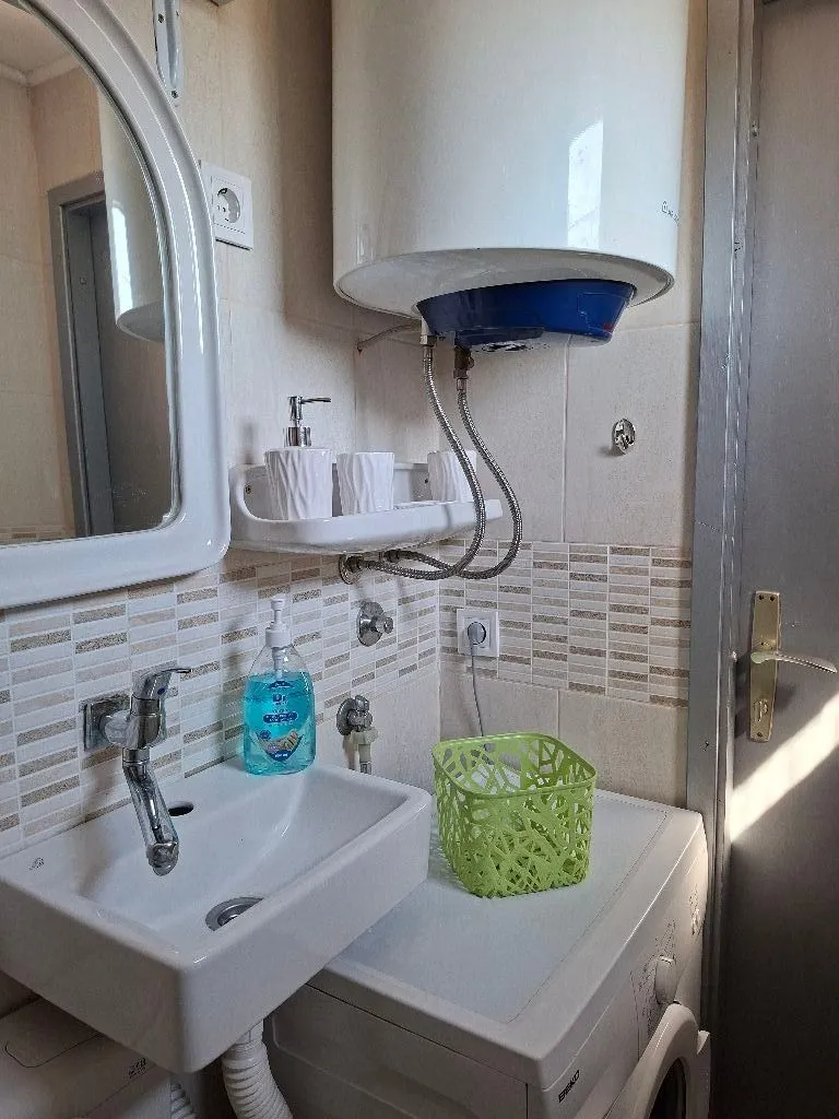 Smaller bathroom with a washbasin, water heater, and washing machine.