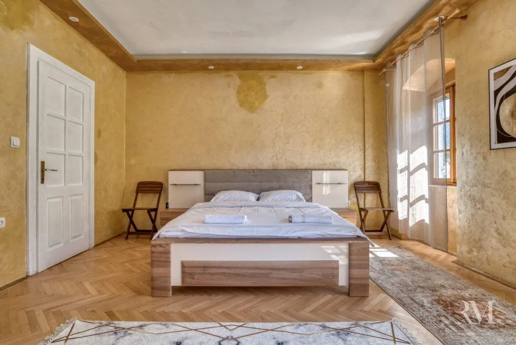 Spacious bedroom with a double bed, wooden flooring, and a window letting in light.