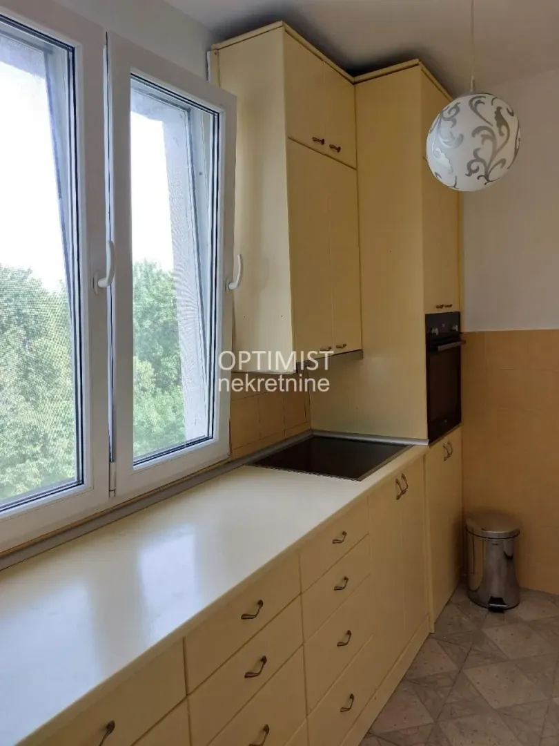 Manja kuhinja sa žutim elementima i prozorom koji gleda na zelenilo.