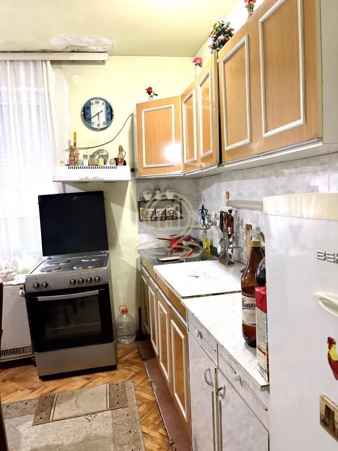 Starija kuhinja sa drvenim elementima, šporetom i frižiderom.