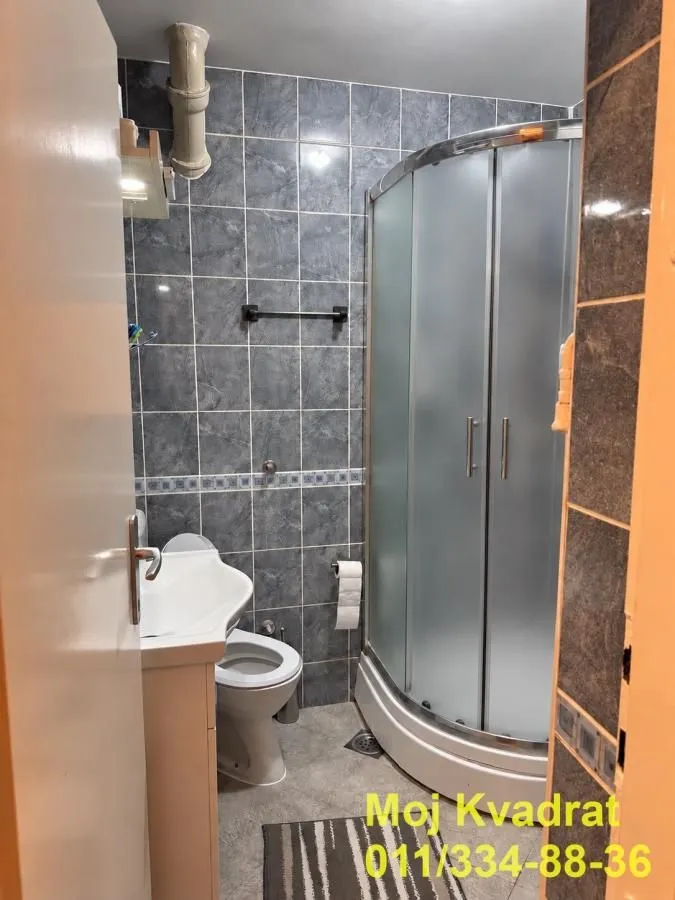 Small bathroom with a shower cabin, washbasin, and toilet tiled with grey-blue tiles.