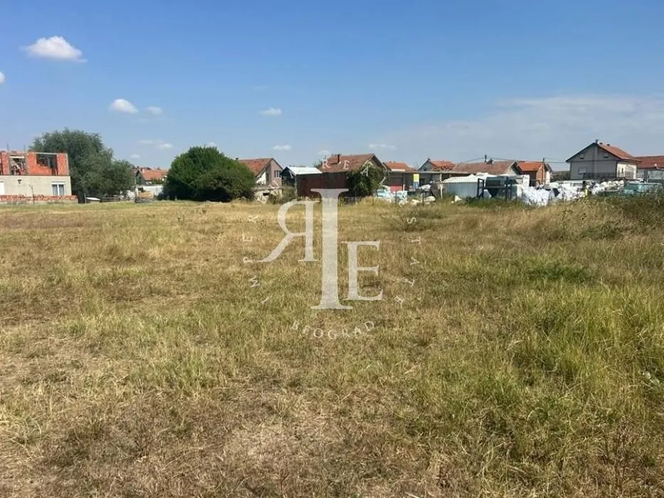 Pogled na ravno građevinsko zemljište obraslo travom sa kućama u pozadini.