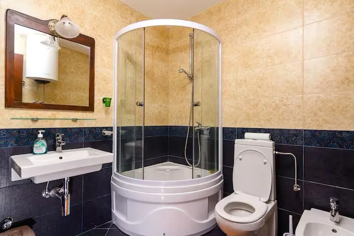 Uređeno kupatilo sa tuš kabinom, umivaonikom, wc šoljom i ogledalom.