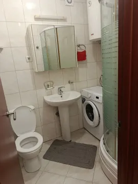 Small bathroom equipped with sanitary facilities, a shower cabin, and a washing machine. - image 9