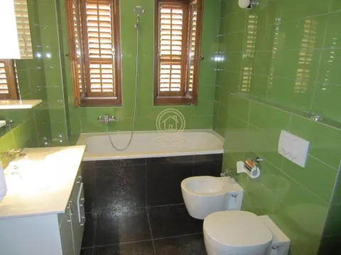 Bathroom tiled in green with a bathtub, sanitary ware, and two windows. - image 7