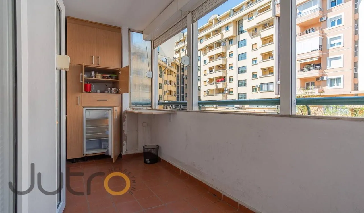 Enclosed balcony with built-in cabinetry and a view of urban buildings.