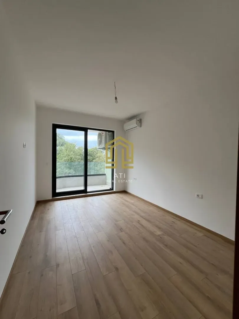 Prazna soba sa parketom, bijelim zidovima i izlazom na terasu.