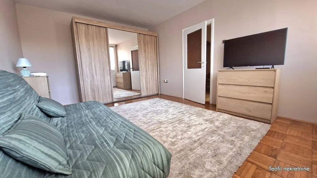 Bedroom with a bed, large wooden wardrobe, chest of drawers, and television.