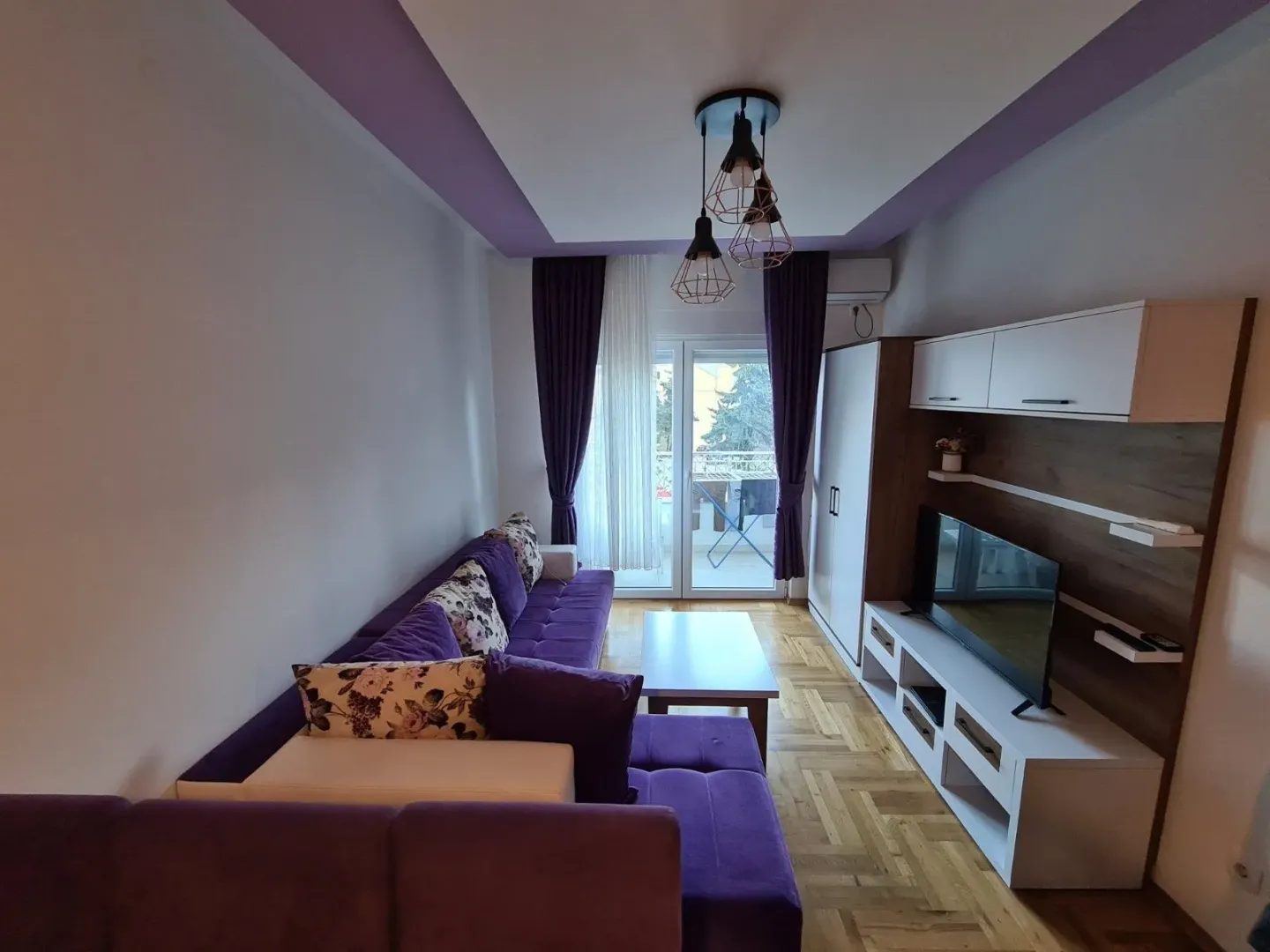Living room with a purple sofa set, TV unit, and access to the terrace.