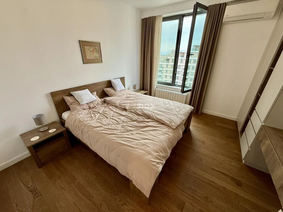 Furnished bedroom with a double bed, wooden flooring, and a window overlooking the city.