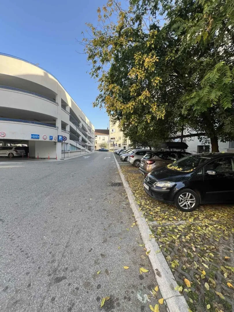 Outdoor parking and a multi-level garage next to a tree-lined street.