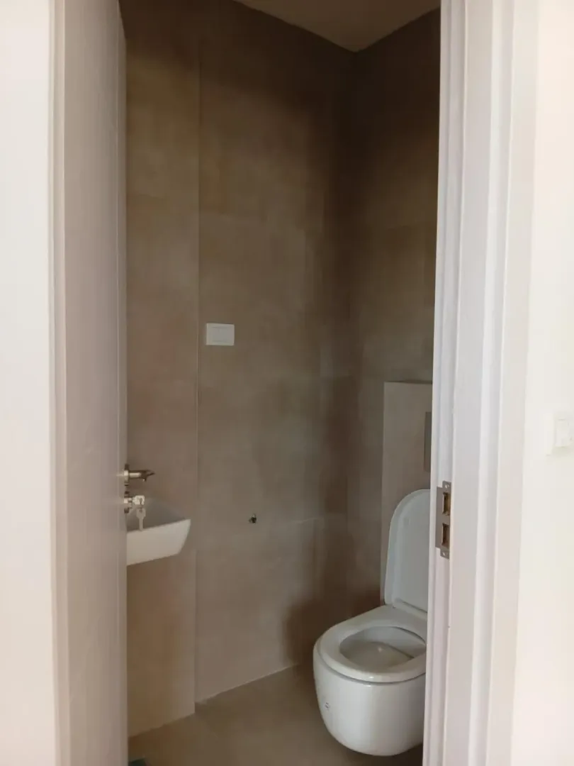 Manje kupatilo obloženo keramičkim pločicama sa toaletom i umivaonikom.