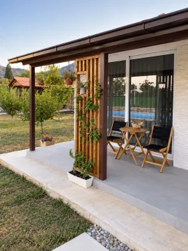 Covered terrace with a wooden table and chairs in front of the house entrance. - image 3