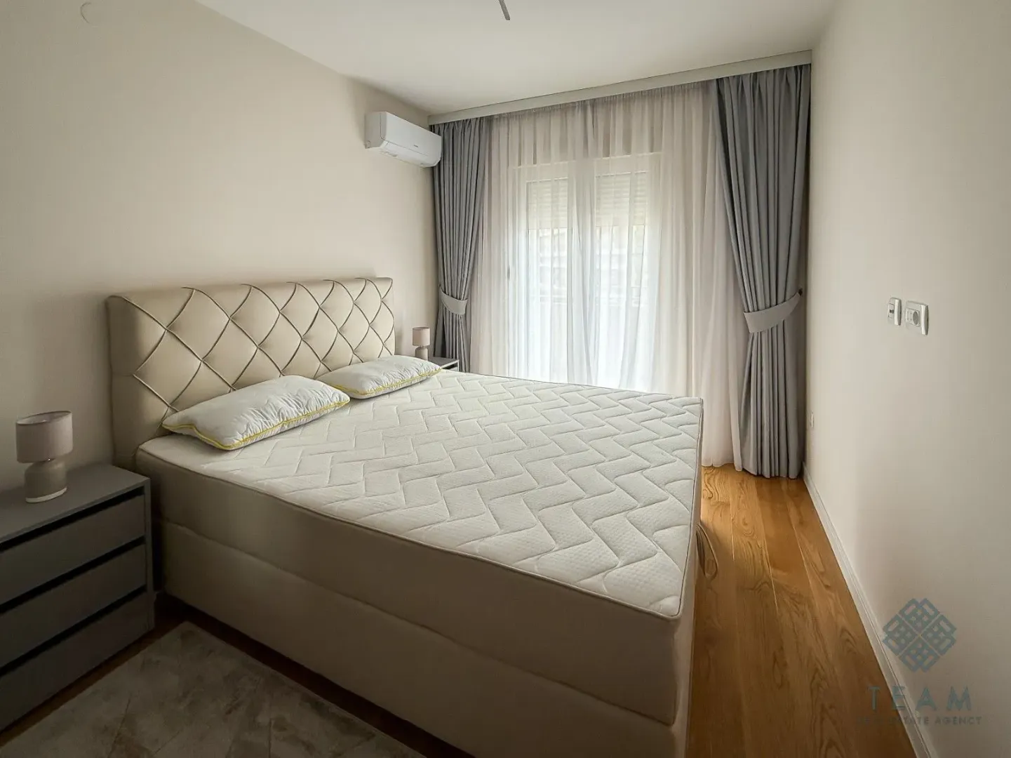 Spacious bedroom with a double bed, wooden flooring, and balcony doors with curtains.