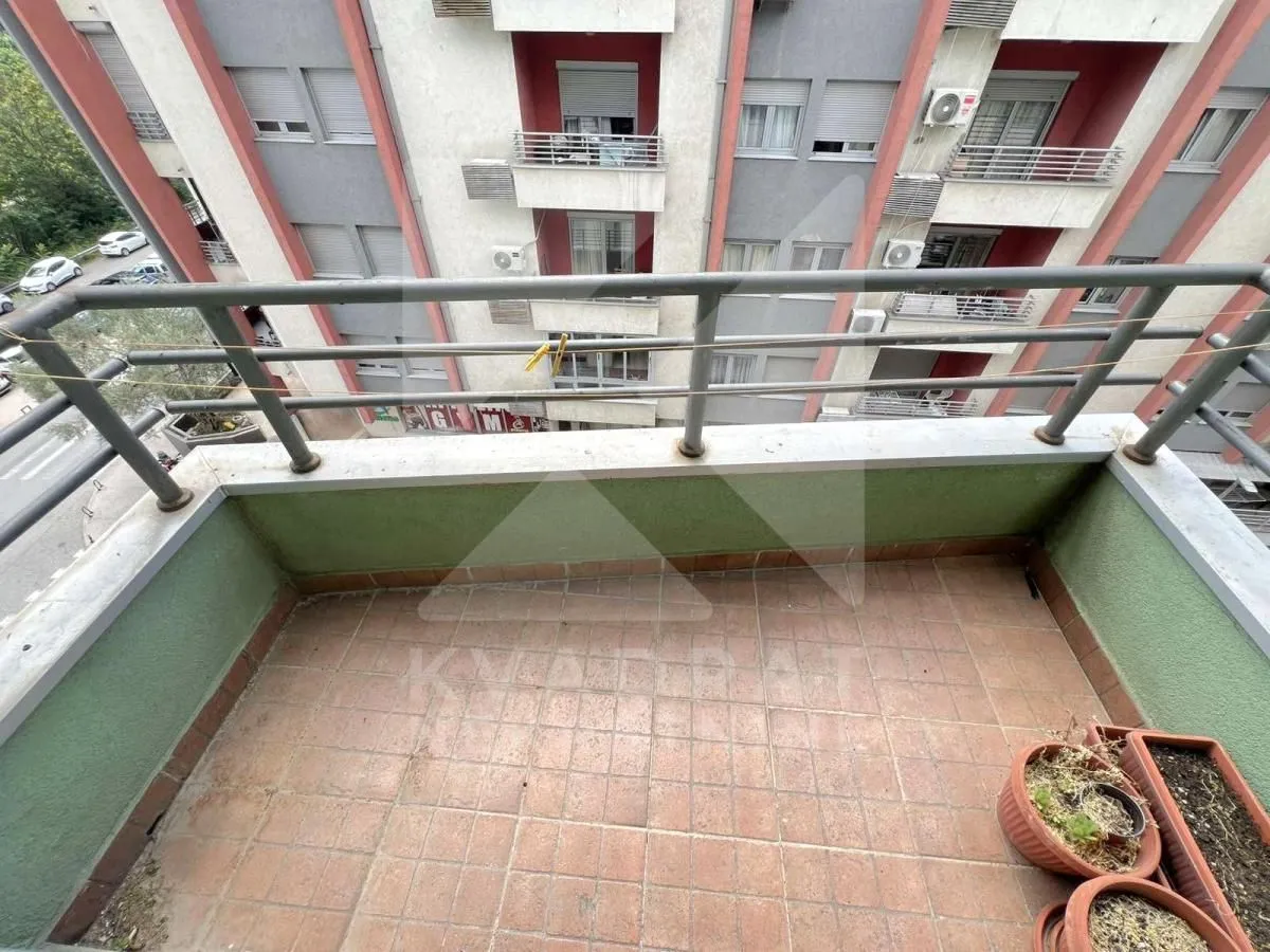 Manji popločani balkon sa metalnom ogradom i pogledom na zgradu.