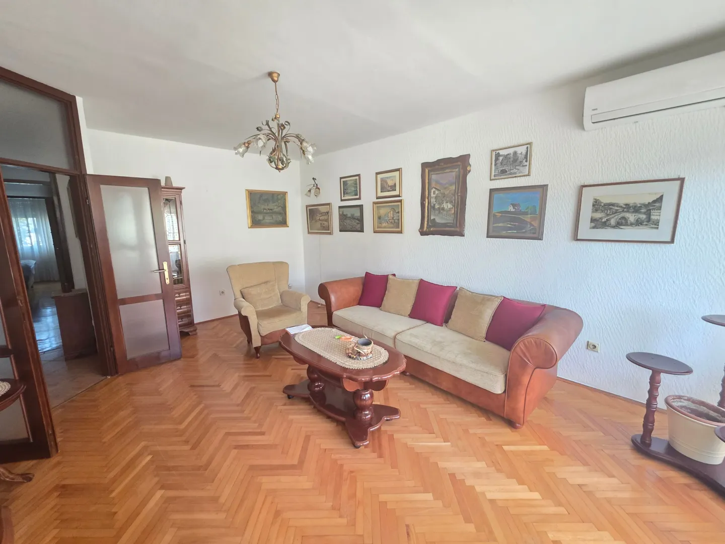 Prostrana dnevna soba sa garniturom, drvenim parketom i umjetničkim slikama na zidu.