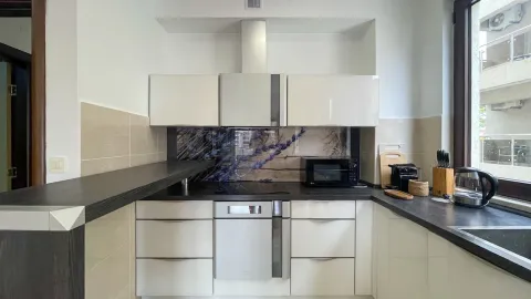 Moderna kuhinja sa bijelim elementima, tamnom radnom površinom i ugradnim aparatima. - image 7