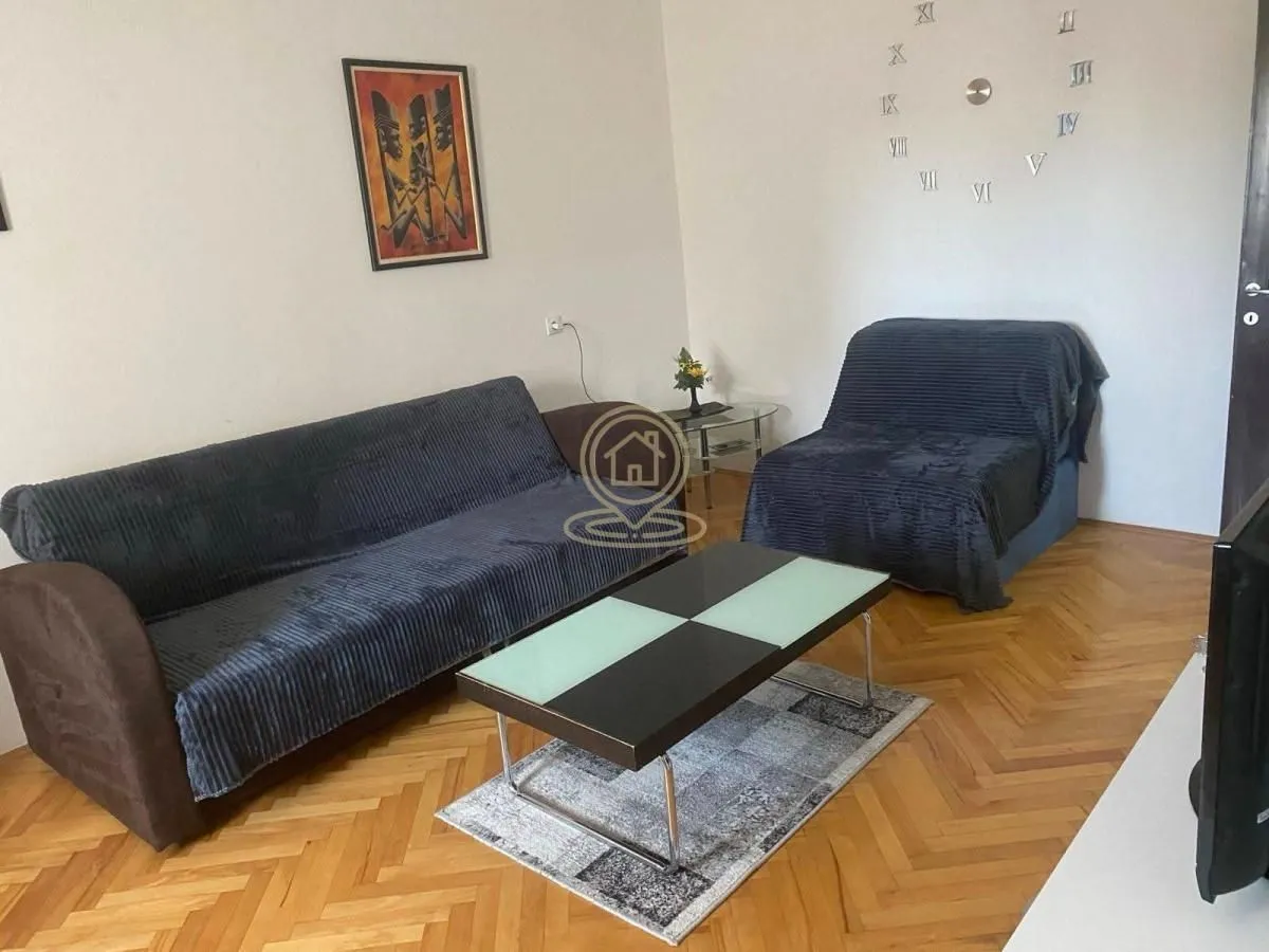 Dnevna soba sa sofom, foteljom, klub stočićem i dekoracijom na zidu.