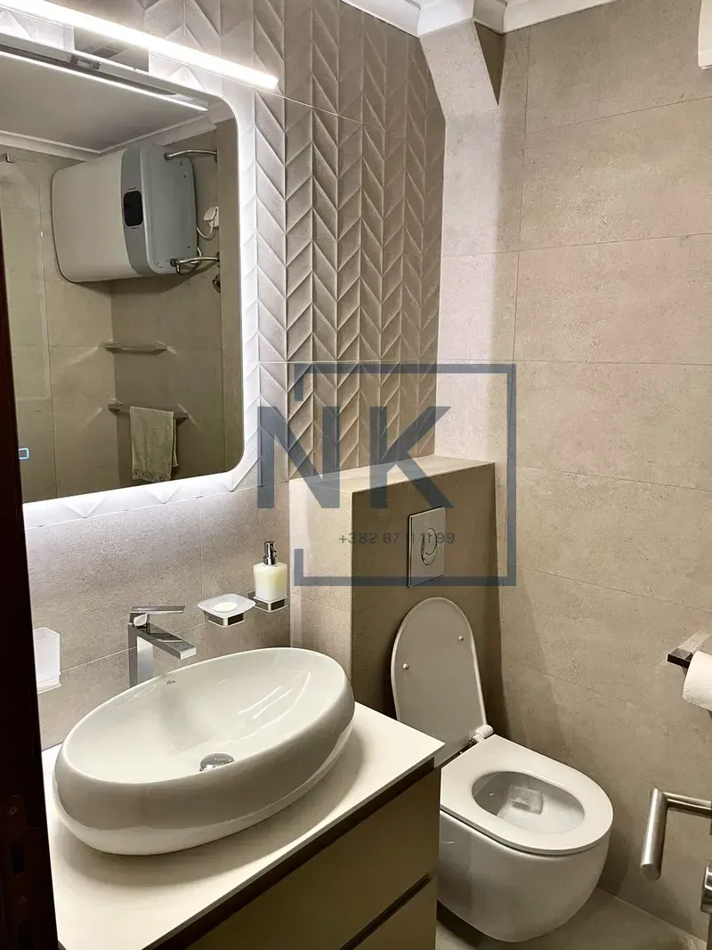 Modern bathroom with a washbasin, toilet, and backlit mirror.