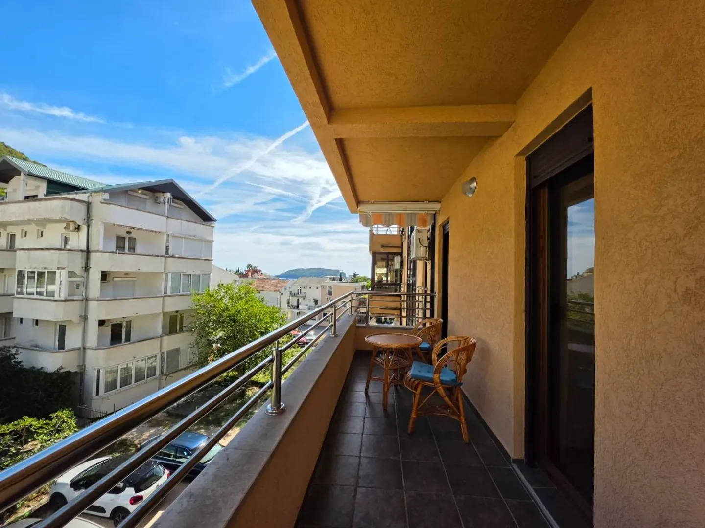 Natkriveni balkon sa garniturom za sjedenje i pogledom na okolne zgrade i naselje.