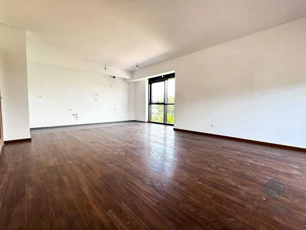 Prazna soba sa tamnim drvenim podom i bijelim zidovima.