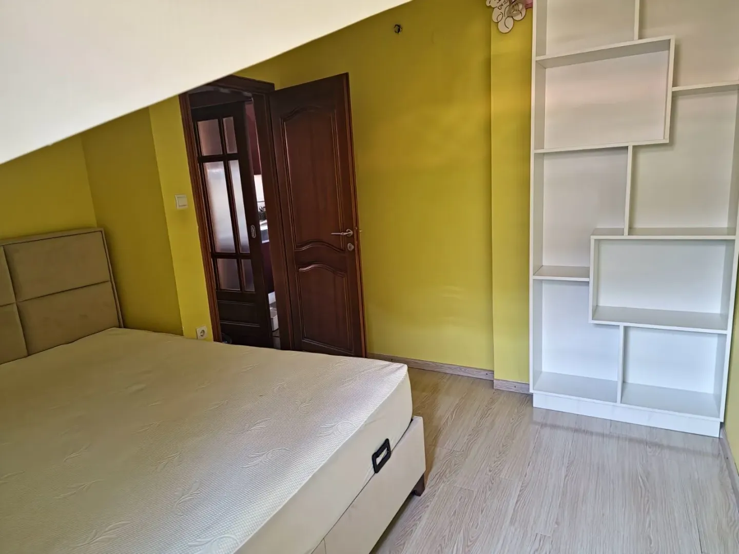A bedroom featuring yellow walls, a bed, and a white shelving unit.