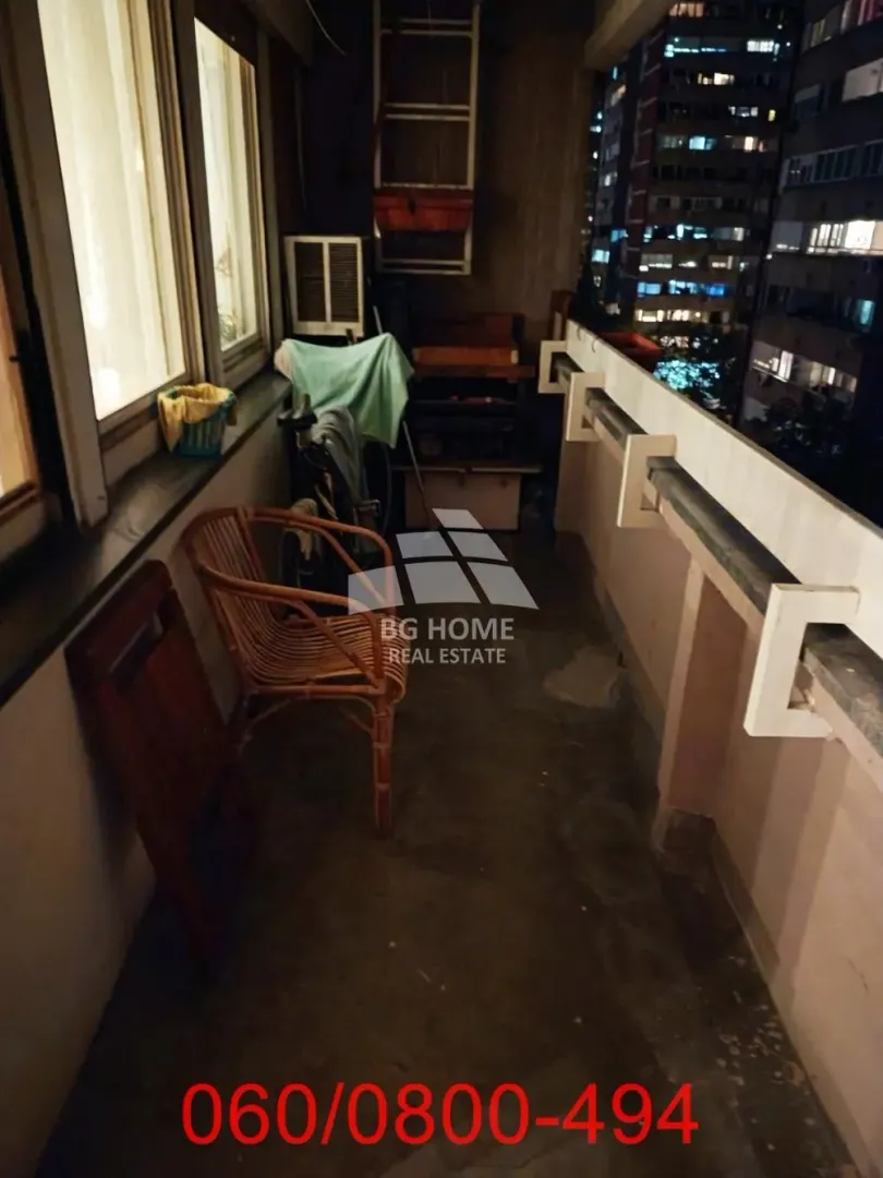 Manji zatvoreni balkon sa stolicom i pogledom na grad noću.