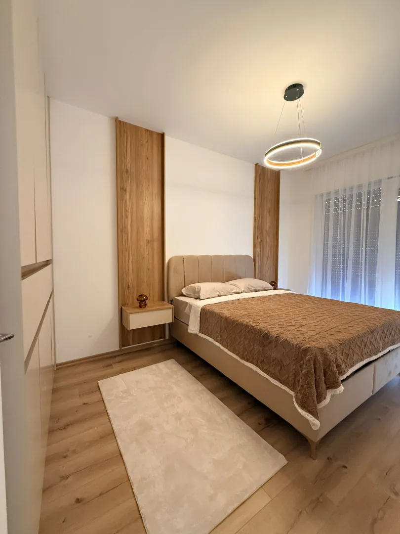 Moderna spavaća soba sa bračnim krevetom, ugrađenim plakarom i dekorativnim osvjetljenjem.