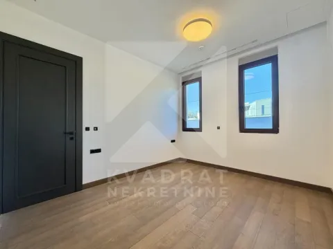 Empty room with wooden flooring, white walls, and two windows. - image 10