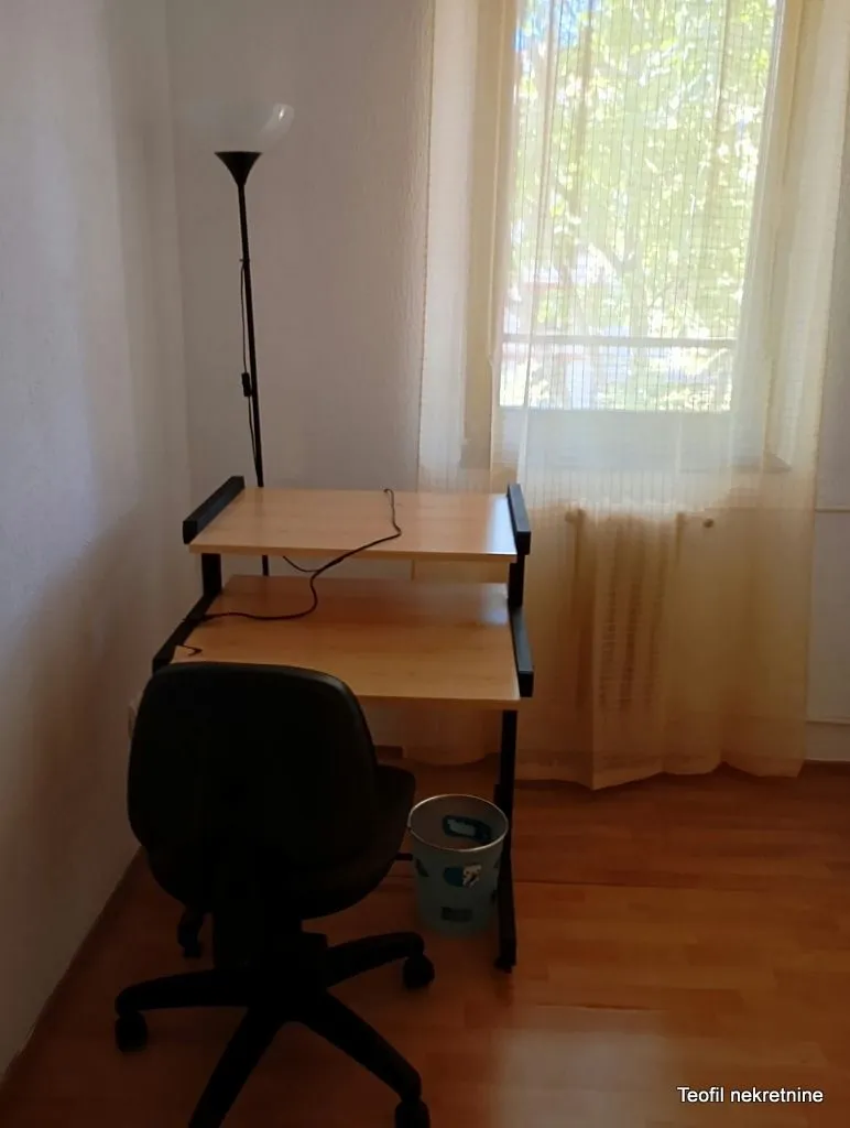 A desk with a chair and a floor lamp near the window.