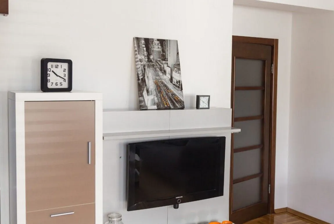 Detalj dnevnog boravka sa TV-om, policama i satovima.