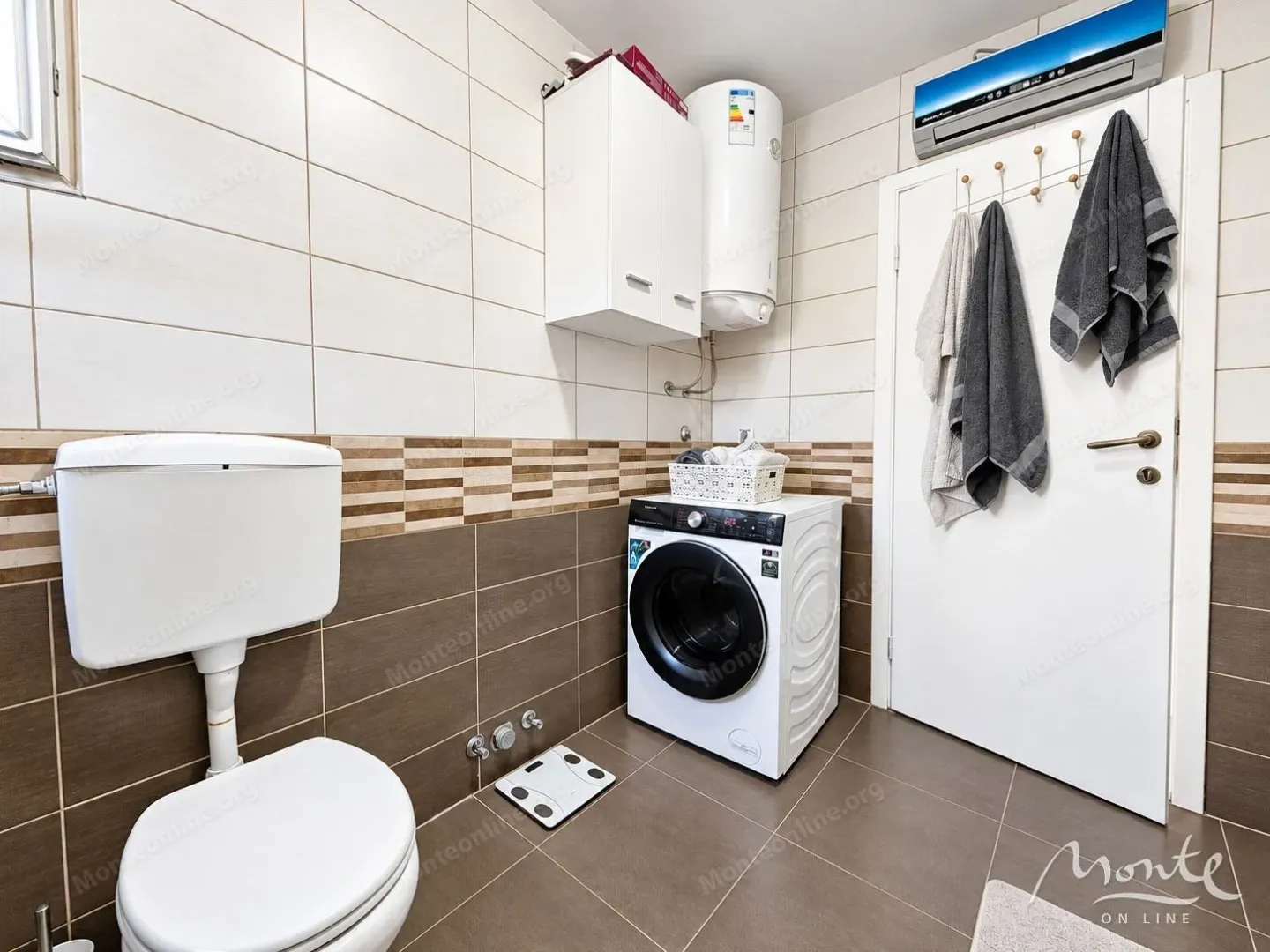 Kupatilo sa wc šoljom, veš mašinom, bojlerom i tuš kabinom.