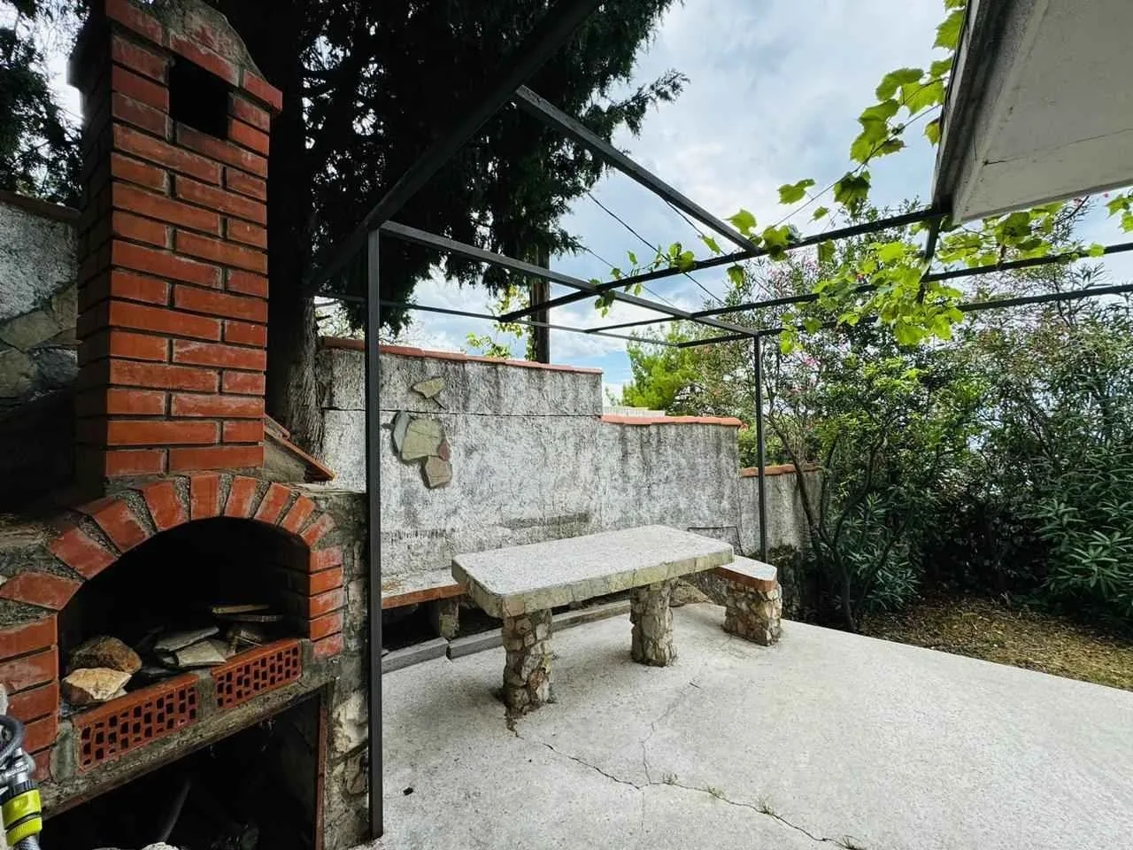 Natkriveni dio dvorišta sa zidanim roštiljem i kamenim stolom.