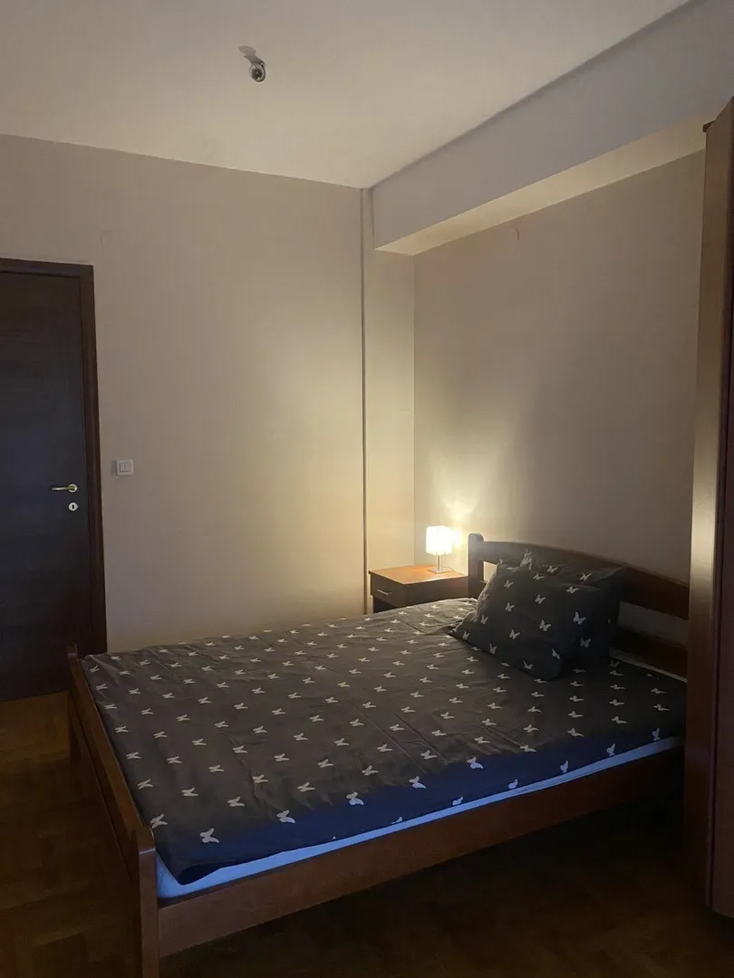A simply furnished bedroom with a wooden bed and a nightstand lamp.