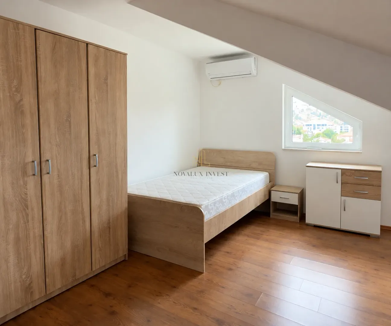 Attic bedroom with a wooden bed, wardrobe, and a small window.
