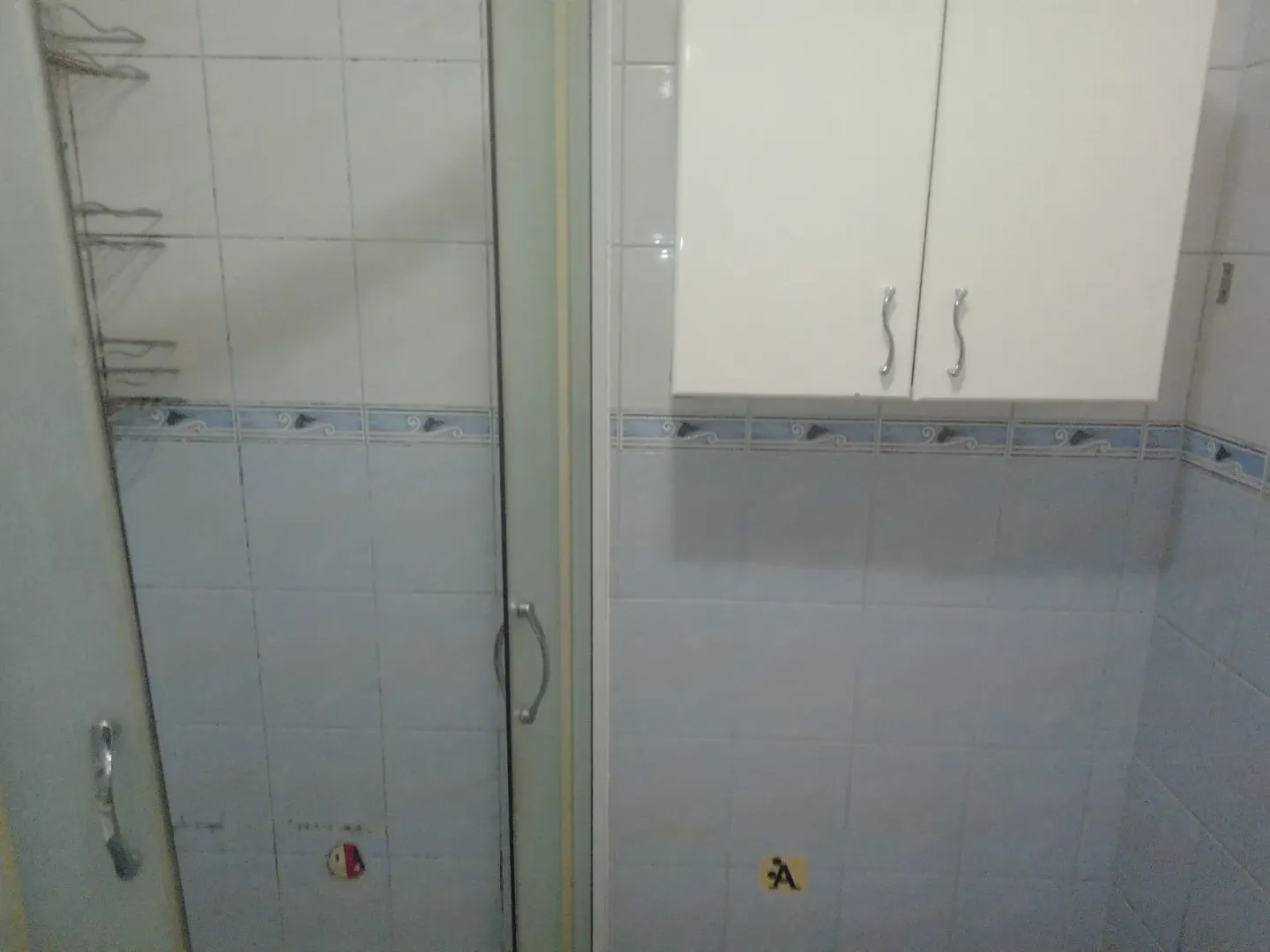 Dio kupatila sa tuš kabinom i bijelim zidnim ormarićem.