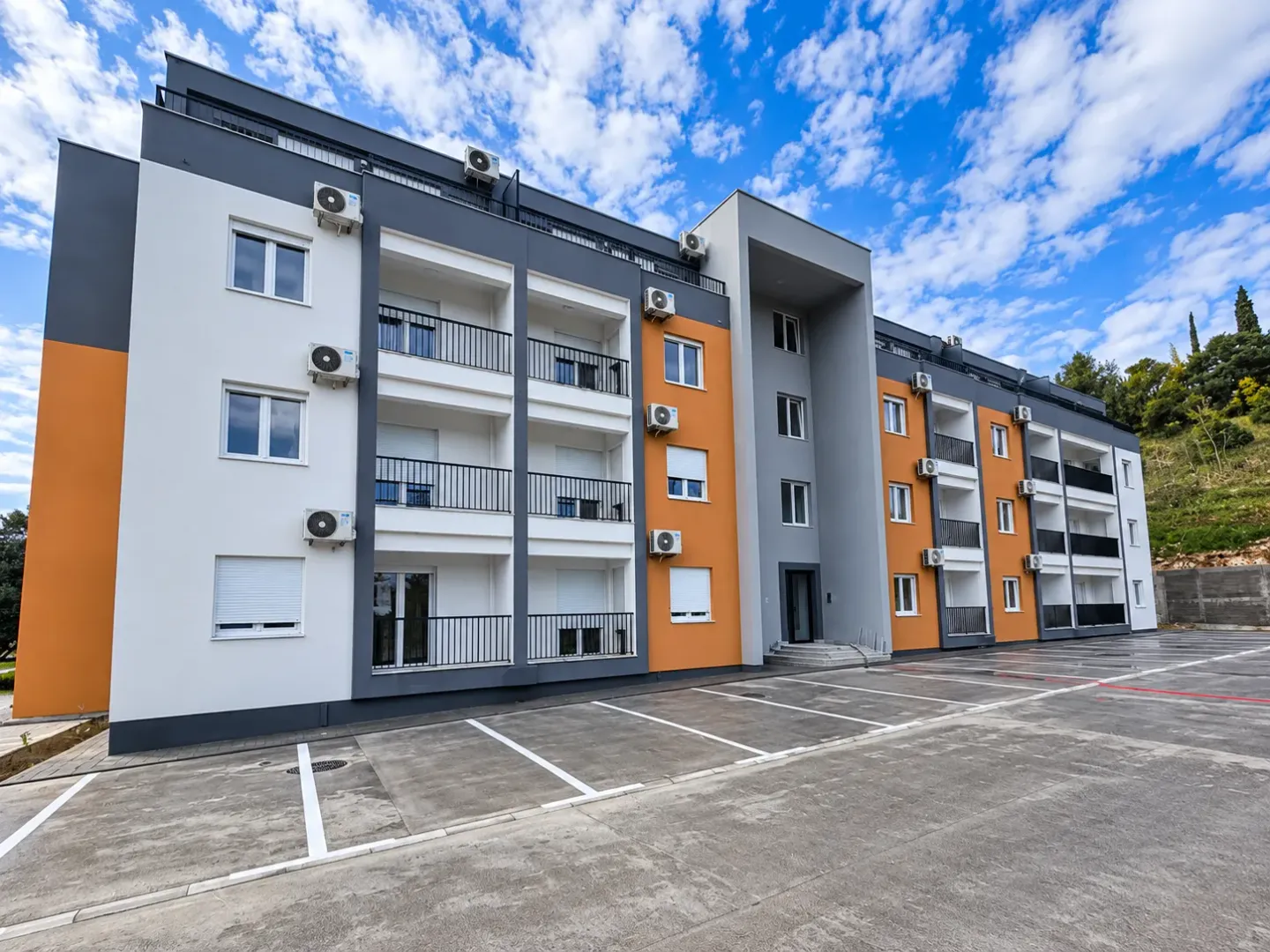 Spoljašnji izgled moderne stambene zgrade sa parkingom ispred.