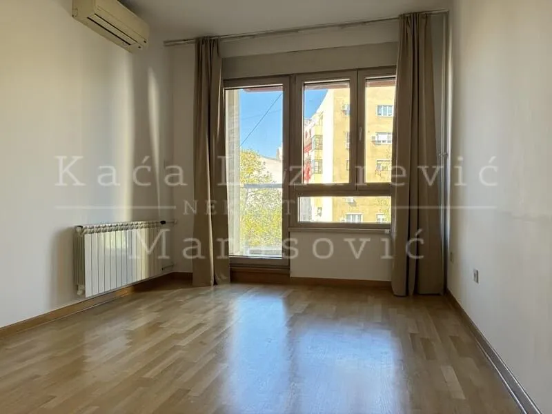 Empty room with wooden flooring, air conditioning, and windows with curtains.