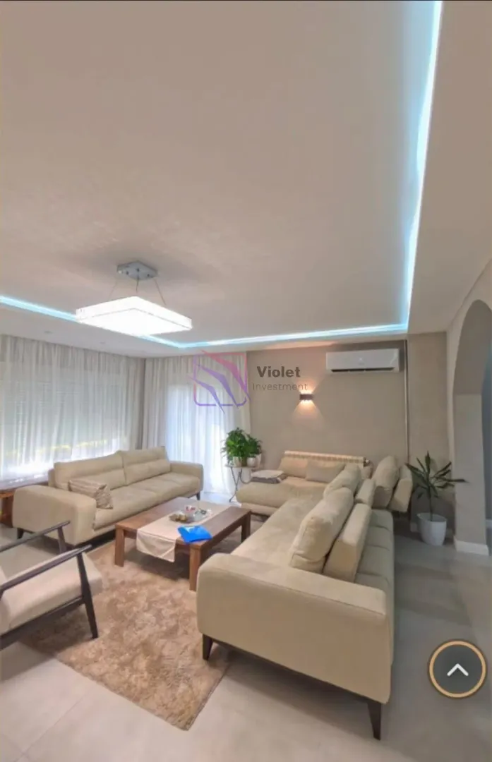 Spacious living room with a seating set and a suspended ceiling with lighting.