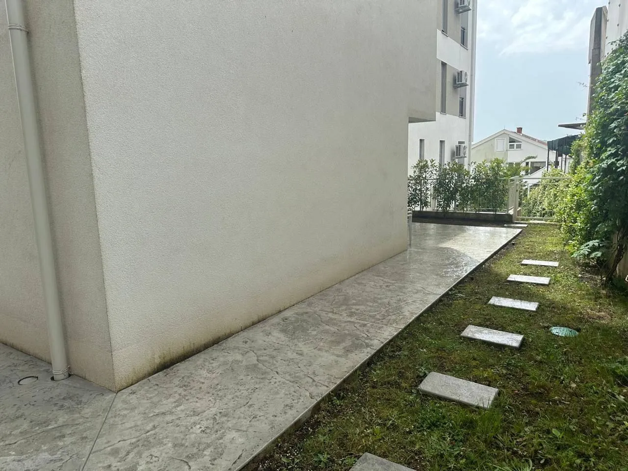 Pogled na popločani dio dvorišta pored zgrade sa travnjakom.